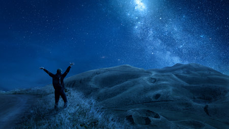 Person with raised arms under a starry night sky in the mountainsの写真素材