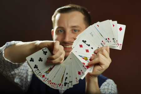 Happy skillful male magician performing playing cards jugglery on dark backgroundの写真素材