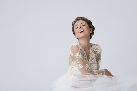 Portrait of happy cheerful bride wearing luxurious wedding dress and spinning over gray background.の写真素材