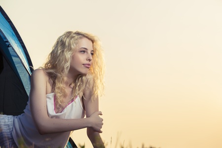 Beautiful blond woman dressed in night wear enjoying the early morning in the entrance of a camping tent.の写真素材