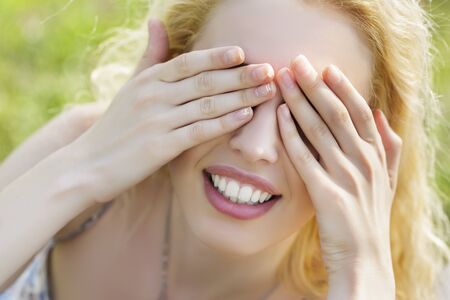Closeup of beautiful playful smiling woman covering her eyes with both her hands. Hide-and-seek.の写真素材