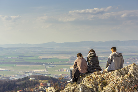 BRASOV, ROMANIA - MARCH 23: Three unidentified young hikers sit on TÃ¢mpa Mountain cliff and enjoy the panorama on March 23, 2014 in Brasov, one of the most visited cities in Romania.のeditorial素材