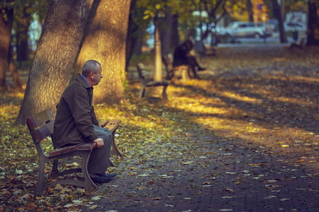 BUCHAREST, ROMANIA - OCTOBER 23, 2013: Unidentified lonely thoughtful retired man on his 60s rests on a bench in a park, autumn scene. The retirees represents 22% of the Bucharestのeditorial素材
