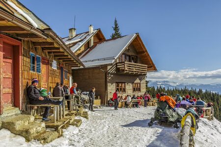 PIATRA CRAIULUI, ROMANIA - FEBRUARY 14, 2015: Unidentified travelers relax and enjoy a winter sunny day at the old wooden Curmatura chalet at 1470m altitude in Piatra Craiului National Park.のeditorial素材
