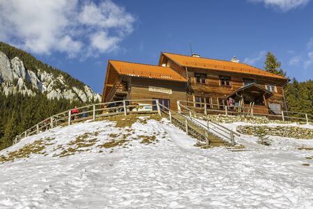 PIATRA CRAIULUI, ROMANIA - FEBRUARY 14, 2015: Unidentified tourists rest and enjoy a winter sunny day at the old wooden Curmatura chalet at 1470m altitude in Piatra Craiului National Park.のeditorial素材