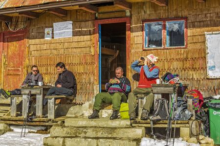 PIATRA CRAIULUI, ROMANIA - FEBRUARY 14, 2015: Unidentified tourists rest on the porch of an old lodging wooden hut at Curmatura chalet at 1470m altitude in Piatra Craiului National Park.のeditorial素材
