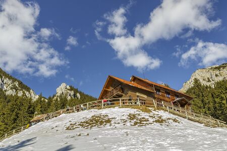 PIATRA CRAIULUI, ROMANIA - FEBRUARY 14, 2015: Unidentified tourists rest and enjoy a winter sunny day at the old wooden Curmatura chalet at 1470m altitude in Piatra Craiului National Park.のeditorial素材