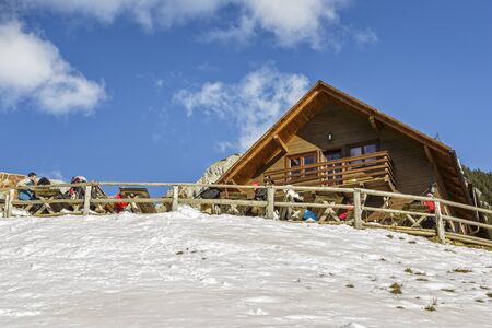 PIATRA CRAIULUI, ROMANIA - FEBRUARY 14, 2015: Unidentified tourists rest and enjoy a winter sunny day at the old wooden Curmatura chalet at 1470m altitude in Piatra Craiului National Park.のeditorial素材