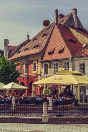SIBIU, ROMANIA - 06 MAY, 2015: Unidentified tourists relax and socialize over a drink in a sidewalk cafe in the Little Square, the second fortified square in the medieval Upper town of Sibiu city.のeditorial素材
