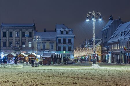 BRASOV, ROMANIA - 6 JANUARY, 2015: Winter urban nightfall scene with tall Christmas decorated lamppost and traditional fair in the snowy Council Square in the old center of Brasov city.のeditorial素材