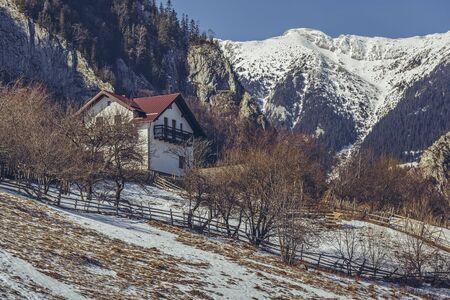 Picturesque rural scenery with snowy Piatra Craiului mountain ridge and vacation house uphill in Magura village, Brasov county, Romania. Vacation destinations.の写真素材