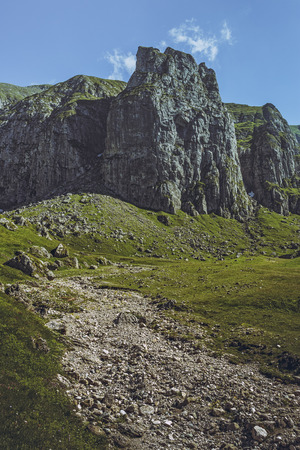 Picturesque mountain landscape with green alpine grasslands, dry riverbed and steep rocky cliffs in the vast Malaiesti Valley in Bucegi mountains, Romania. Romanian travel destinations.の写真素材