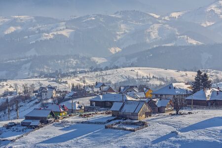 Countryside landscape with traditional Romanian village in the valleys of the Bucegi mountains on a sunny cold winter morning in Pestera, Brasov county, Transylvania region, Romania.の写真素材