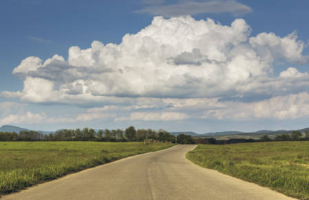 Summer countryside landscape with stormy cumulonimbus clouds in the sky and empty road crossing the grasslands of the Transylvania region, Romania.の写真素材