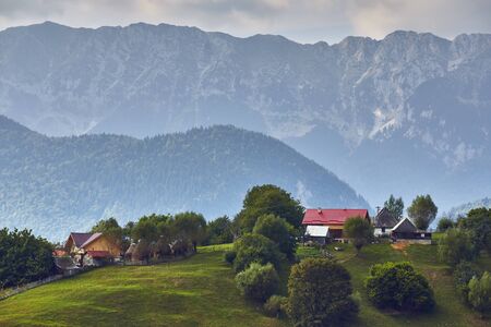 Springtime rural landscape with Romanian village on a green hill near Piatra Craiului Mountain range, in Magura, Brasov county, Transylvania, Romania.の写真素材