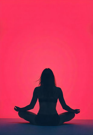 A silhouette of a man meditating in the lotus position, set against a large, glowing sun in a deep pink and red sky. The minimalist scene conveys peace and introspection.の素材