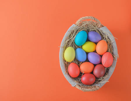 colorful easter eggs in a basket with hay on an orange backgroundの写真素材