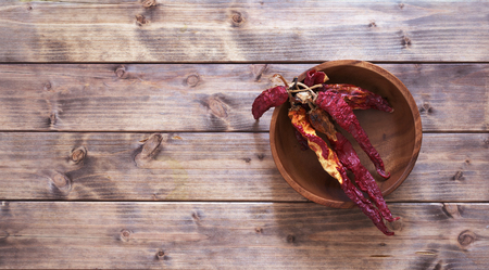 dry red peppers on a wooden table in a wooden bowlの写真素材