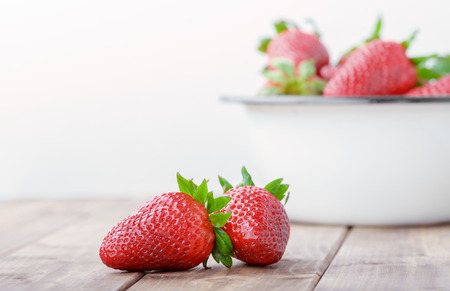 two strawberries closeup on the foreground on the background of a full bowl of strawberriesの写真素材