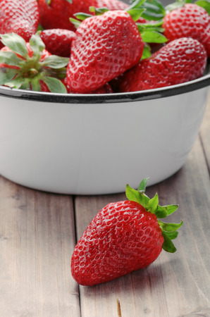 strawberry closeup on the foreground on the background of a full bowl of strawberriesの写真素材