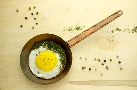 Fried egg in a copper pan on a wooden boardの写真素材