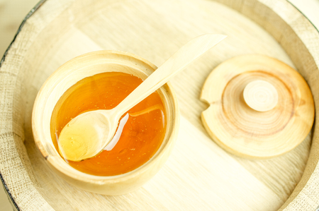Honey in a wooden bowl with a wooden spoon and lid. Background wooden barrelの写真素材