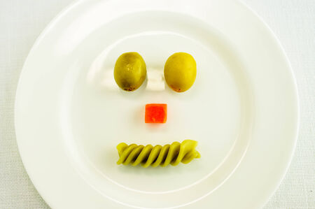 Smile of olives, carrots and pasta on a white plateの写真素材