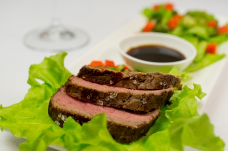 Roasted beef meat with vegetables on a lettuce leaf. Sauce and a glass of wine background.