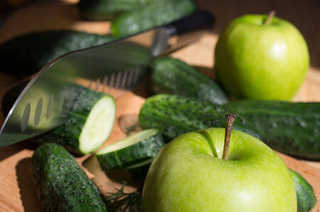 Cucumbers cut knife on a wooden board and dill and apple.の写真素材