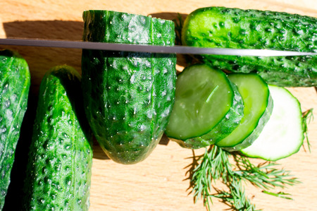 Cucumbers cut knife on a wooden board and dill.の写真素材