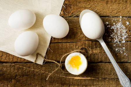 Chicken eggs raw and cooked boiled on old boardsの写真素材