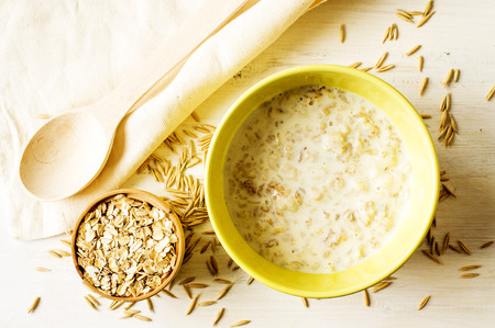 Oat milk porridge in a yellow bowl on the table with oatsの写真素材