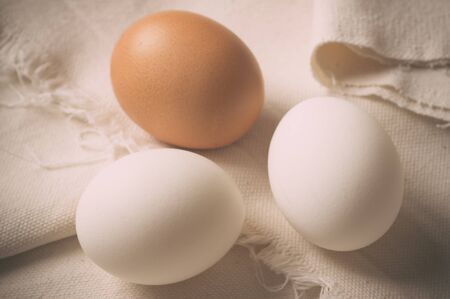 Three eggs - two white and one brown on rough fabric. Pastel filterの写真素材