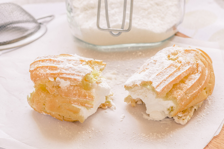 Cake eclair custard is broken in half on a table with a jar of powdered sugar