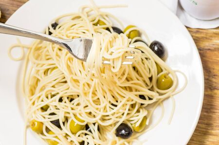Italian dish of spaghetti with olives and oil and forkの写真素材