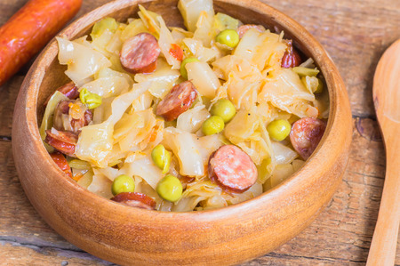 Cabbage stew with sausage and peas in a wooden bowlの写真素材