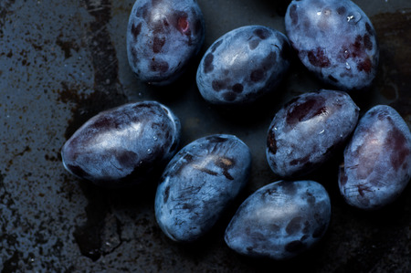 Ripe plums on a black background with water dropsの写真素材