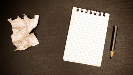 On the brown office table is a small notebook, a simple pencil and a crumpled sheet from a notebookの写真素材