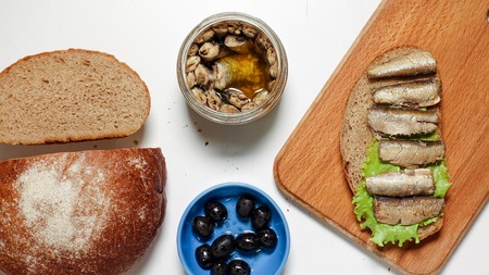 Sardines, sprats on a piece of black bread with a leaf of lettuce on a board, near black bread,...