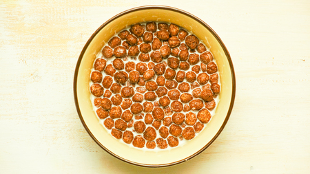Ready breakfasts chocolate balls in a bowl of milk, top view, on a white table