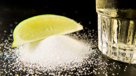 A pile of salt with a lime slice and a glass of cold tequilaの写真素材