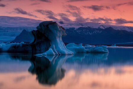The Jökulsárlón is a large glacial lake in southeast Iceland, the floating ice floes on a quiet surface of gracial lagoon, a dramatic sunset sky is reflected on the surfaceの写真素材