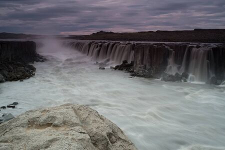 The Sellfoss Waterfall with golden clouds in the sky. The flowing water is captured by a long...
