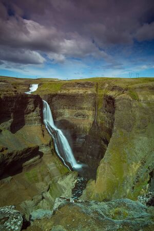 The Haifoss Waterfall with golden clouds in the sky. The flowing water is captured by a long exposure. Amazing blue color of water from the glacier. Natural and colorful environment.の写真素材