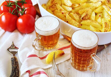 Fried potatoes with spices, tomatoes and two mugs of beerの写真素材