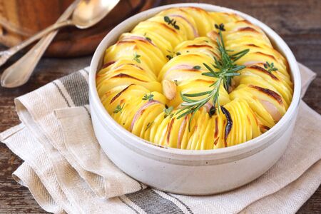 Slices of fried potatoes with onions, garlic and rosemary in ceramic potの写真素材
