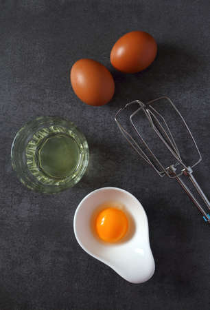 Egg beater and  broken egg on dark background