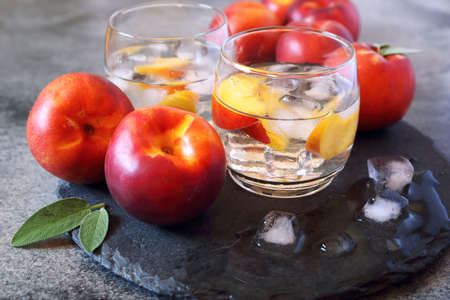 Summer diet cold drink: detox pure water with nectarine and ice, two glasses on dark backgroundの写真素材