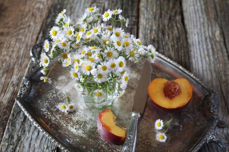 Summer composition: bouquet of field daisies and ripe nectarine on vintage trayの写真素材