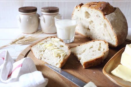 French sourdough bread, butter and glass of milk on wooden chopping boardの写真素材